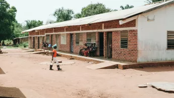 Ein flacher Gebäudetrackt, davor Sandweg und ein laufende Person.