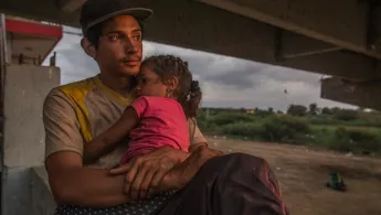 Foto eines jungen Mannes, der seine Tochter im Arm hält Flucht: junger Mann mit Tochter auf Arm