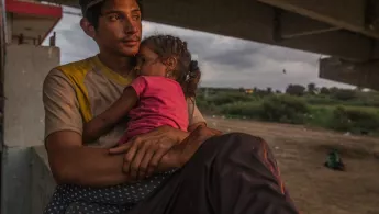 Foto eines jungen Mannes, der seine Tochter im Arm hält Flucht: junger Mann mit Tochter auf Arm