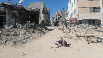 Junge sitzt auf Sandstraße in zerstörter Stadt