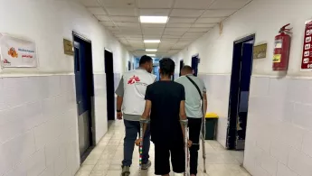 Mitarbeitende und Patient auf Krücken in Krankenhausgang