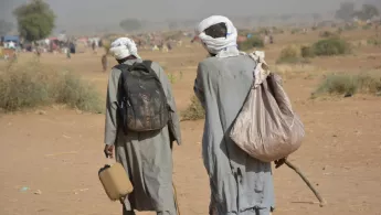 Zwei Männer gehen schwer bepackt durch eine trockene Landschaft