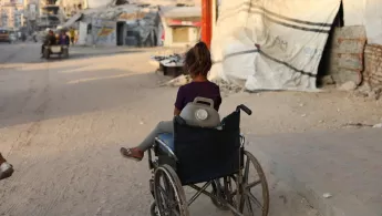 Kleines Mädchen sitzt in Rollstuhl mit Wasserkanister