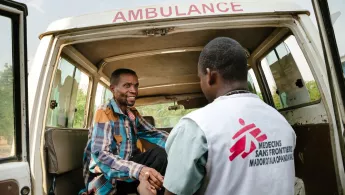 Ein Patient mit HIV wird zur weiteren Behandlung in ein Krankenhaus gebracht. Ein Mitarbeiter hilft einem Patienten an Bord eines Krankenwagens