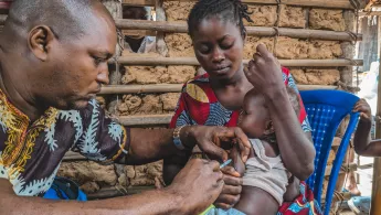 Mitarbeiter gibt Kleinkind auf Schoß von Mutter eine Spritze