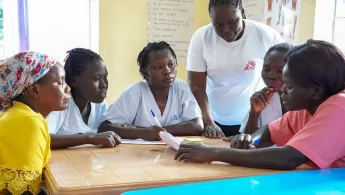 Mitarbeitende sitzen an Tisch, eine Person spricht.