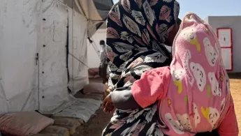 Frau mit Kopftuch hält Kind auf dem Arm