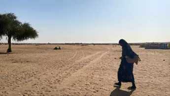 Eine Frau geht alleine über eine freie sandige Fläche.