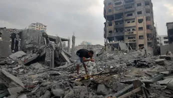 Ein Mensch an Wasserleitung zwischen den Trümmern zerstörter Gebäude