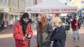 Drei Personen reden vor einem Ärzte ohne Grenzen Info-Stand