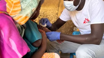 Mitarbeiter impft ein Kind welches im Arm der Mutter liegt