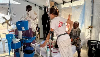 Mitarbeiterin und Angehörige an Bett von Kleinkind