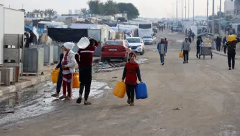 Palästinensische Männer und Kinder tragen Wasserkanister.
