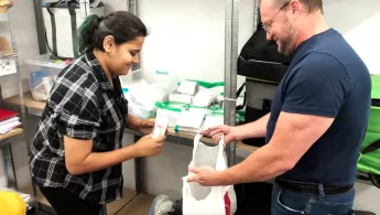 Eine Frau und ein Mann stehen sich gegenüber und der Mann hält der Frau eine Plastiktüte auf.
