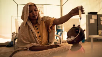 Eine Mutter sitzt auf einem Krankenbett und gibt ihrer Tochter therapeutische Milch