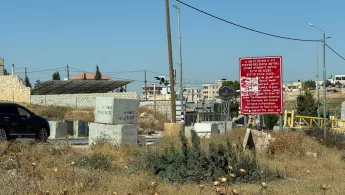 Mehrere Betonblöcke versperren eine Straße neben einem roten Warnschild; im Hintergrund stehen Häuser.