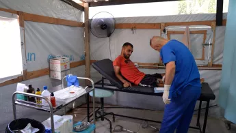 Ein Patient wird auf einer Liege in einem Zelt behandelt.
