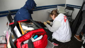 Eine Mitarbeiterin von Ärzte ohne Grenzen versorgt mit Handschuhen das Knie einer sitzenden Person, während im Vordergrund eine geöffnete rote Notfalltasche steht.