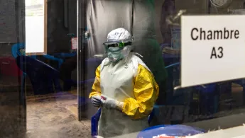 Eine Person trägt Schutzkleidung hinter einer Scheibe