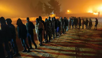 Zahlreiche Menschen stehen in der Dämmerung in einer langen Schlange