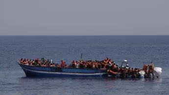 232 in Seenot geratene Menschen mit Rettungswesten auf einem Holzboot im Mittelmeer