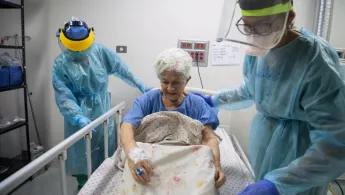 Alte Frau wird von zwei Pflegern in Schutzkleidung betreut