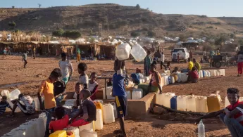 Menschen stehen mit Kanistern an einer Wasserversorgung an 