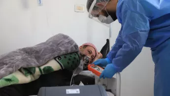 Ein Mann in blauem Schutzanzug beugt sich zu einem Mann herunter, der künstlich beatmet wird