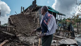 Person vor zerstörtem Haus