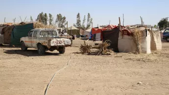 Ein altes Auto vor einem Camp mit vielen Zelten in einer wüstenähnlichen Landschaft