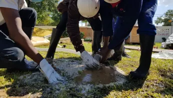 Drei Mitarbeitende von Ärzte ohne Grenzen mit Helmen buddeln ein Loch