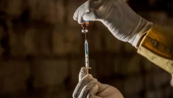 Zwei Hände die Impfstoff in eine Spritze ziehen