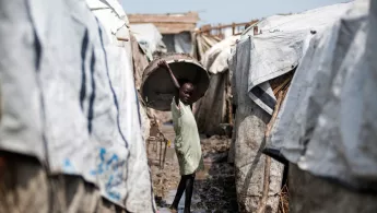 Ein Mädchen hält einen großen Korb über ihren Kopf, während sie zwischen mehreren Zelten steht