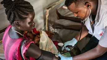 Ein Pfleger misst bei einer Mutter mit Neugeborenem den Blutdruck