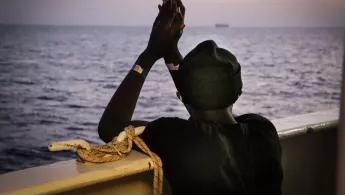 An der Reling der Sea Watch 4 schaut eine gerettete Person aufs Meer