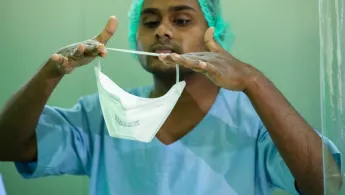 Mann in OP-Kleidung zieht FFP2-Maske an