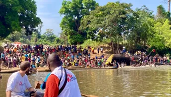 Zwei Männer auf Boot fahren ans Ufer zu Menschengruppe