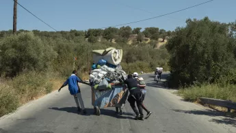 Geflüchtete laufen auf einer Straße, in ihrer Mitte ein Wagen mit Ihrem Hab und Gut.