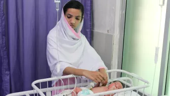 Krankenpflegerin behandelt Neugeborenes in Kinderbett