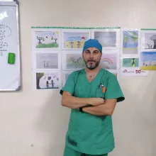 Davide Musardo vor einer Wand mit Kinderbildern in OP-Kleidung