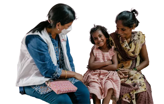 Ein junges Mädchen schaut lächelnd in die Kamera, links von ihr eine Mitarbeiterin und rechts von ihr ihre Mutter die sie ihm Arm hält