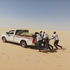 Unsere Mitarbeitenden schieben ein Auto in der Wüste an.
