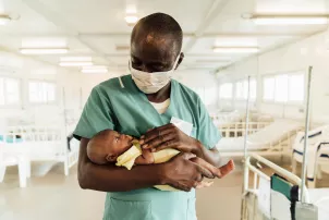 Ein Krankenpfleger in Sierra Leona hält ein Neugeborenes.
