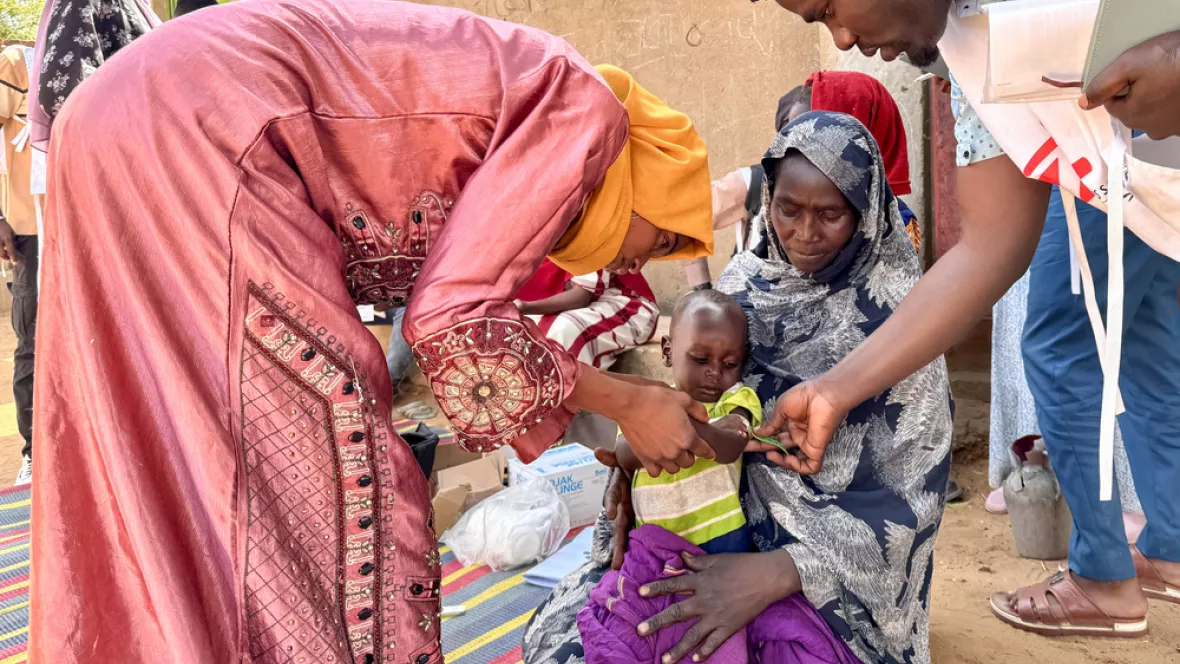 Mitarbeitende messen Armumfang von kleinem Jungen auf Schoß von Mutter