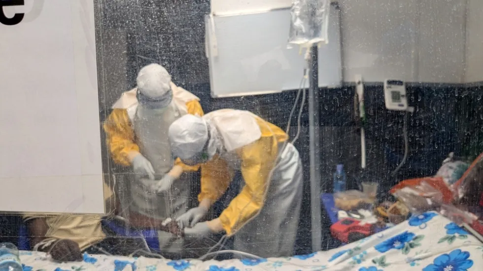 Zwei Menschen in Schutzbekleidung untersuchen eine erkrankte Person