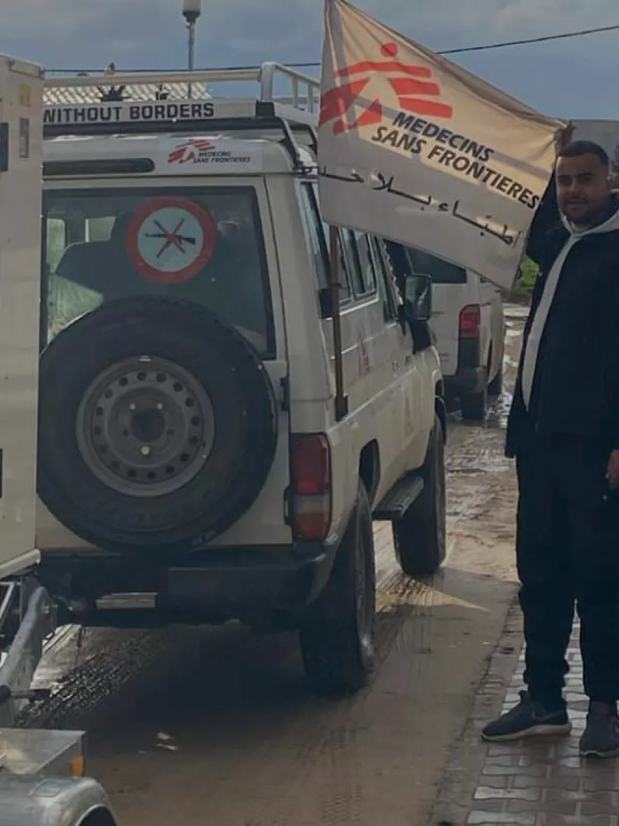 Mitarbeitender steht neben Fahrzeug mit Flagge von Ärzte ohne Grenzen