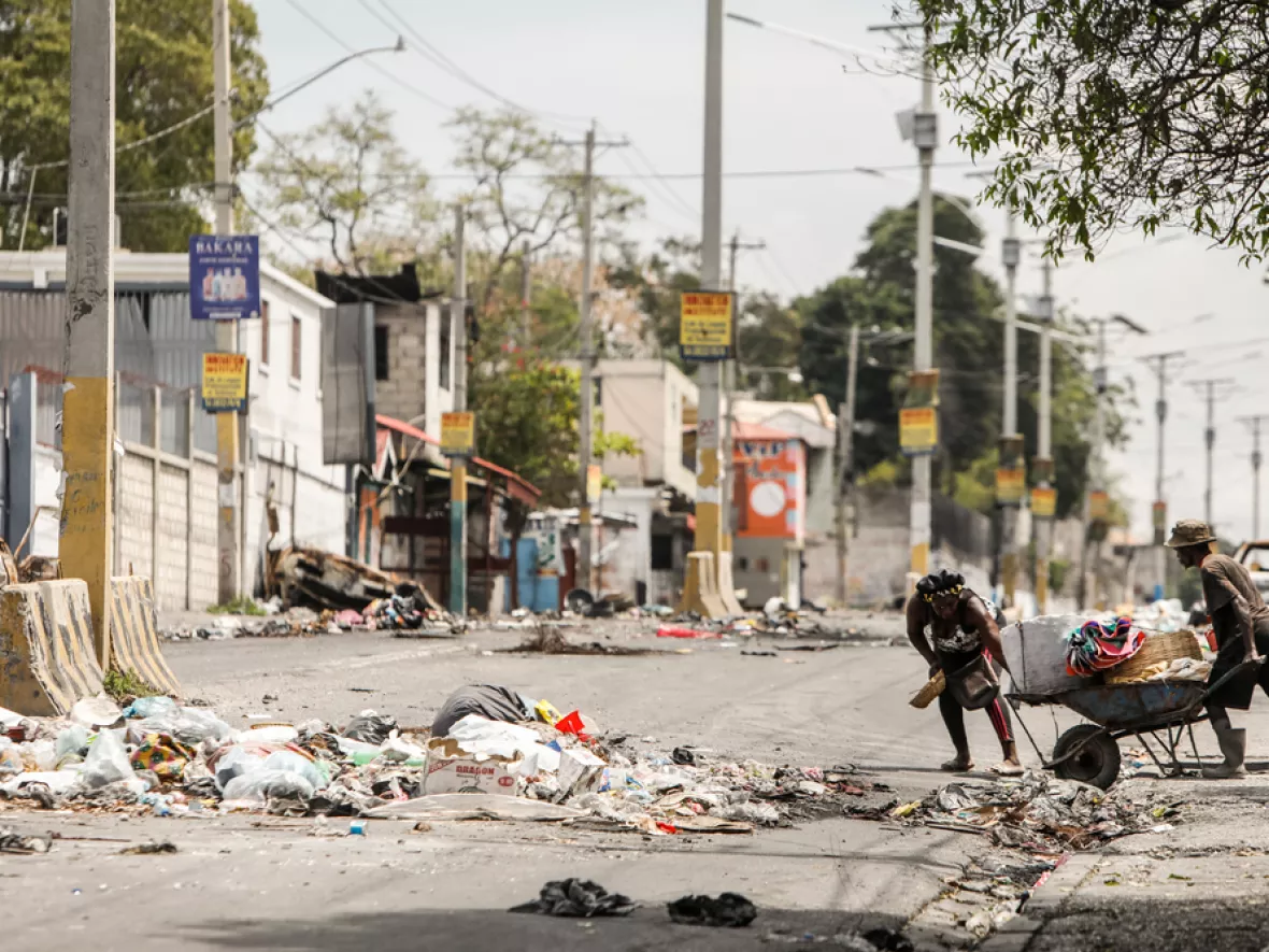 Eine Schubkarre wird von zwei Menschen über die Straße geschoben.