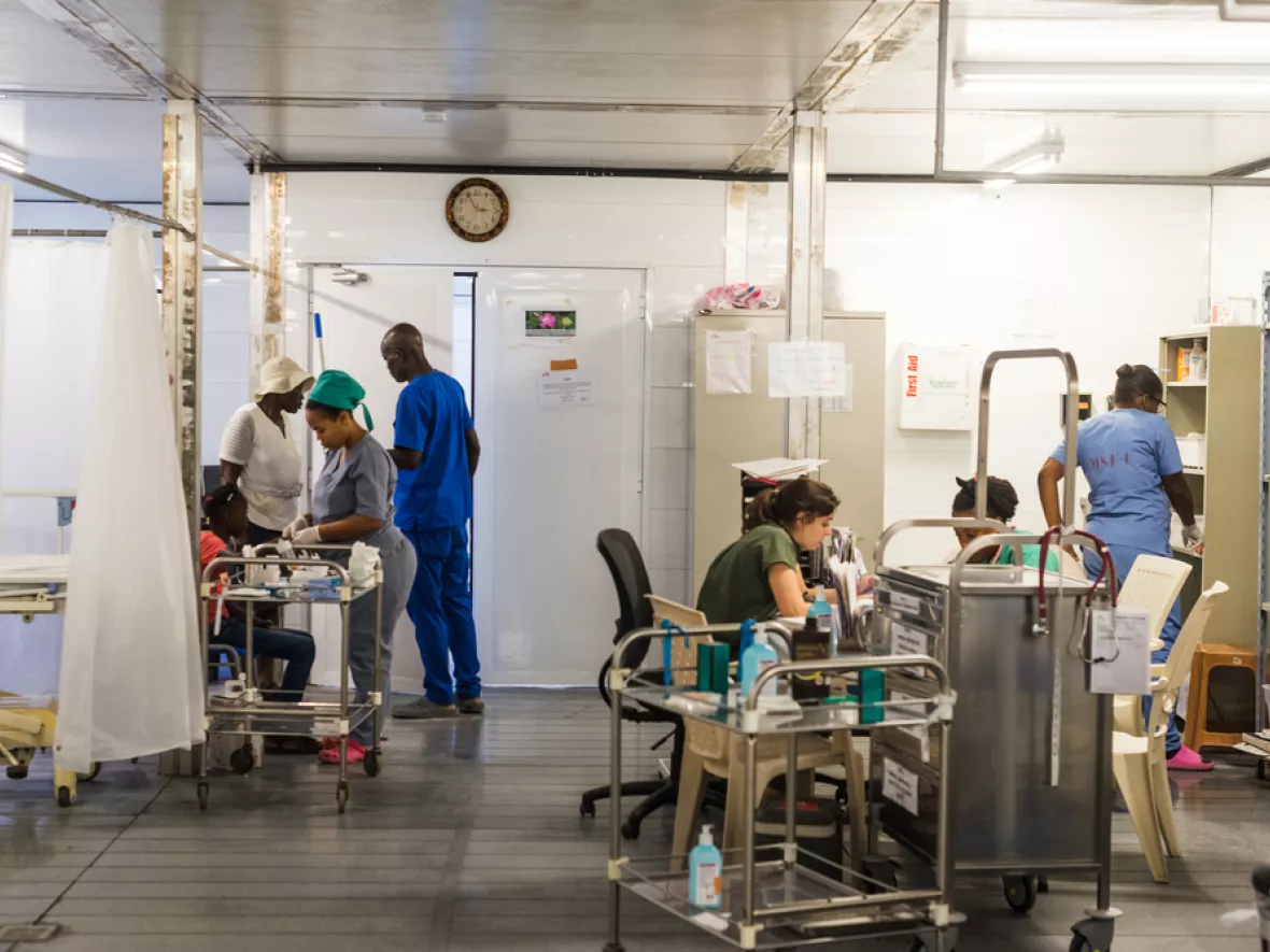 Menschen stehen in der Notaufnahme und Patient*innen werden behandelt.