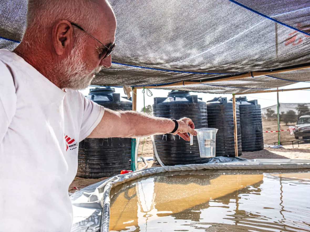 Mitarbeitender hebt Wasser aus Sammelbecken im Camp Metche