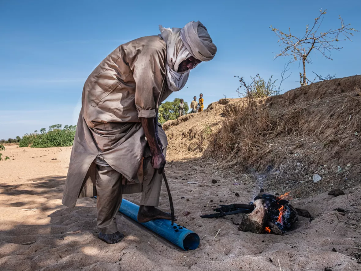 Person brennt Löcher in Plastikrohr in trockenem Flussbett